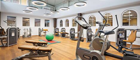 A gym with various exercise equipment, wooden flooring, and large windows.