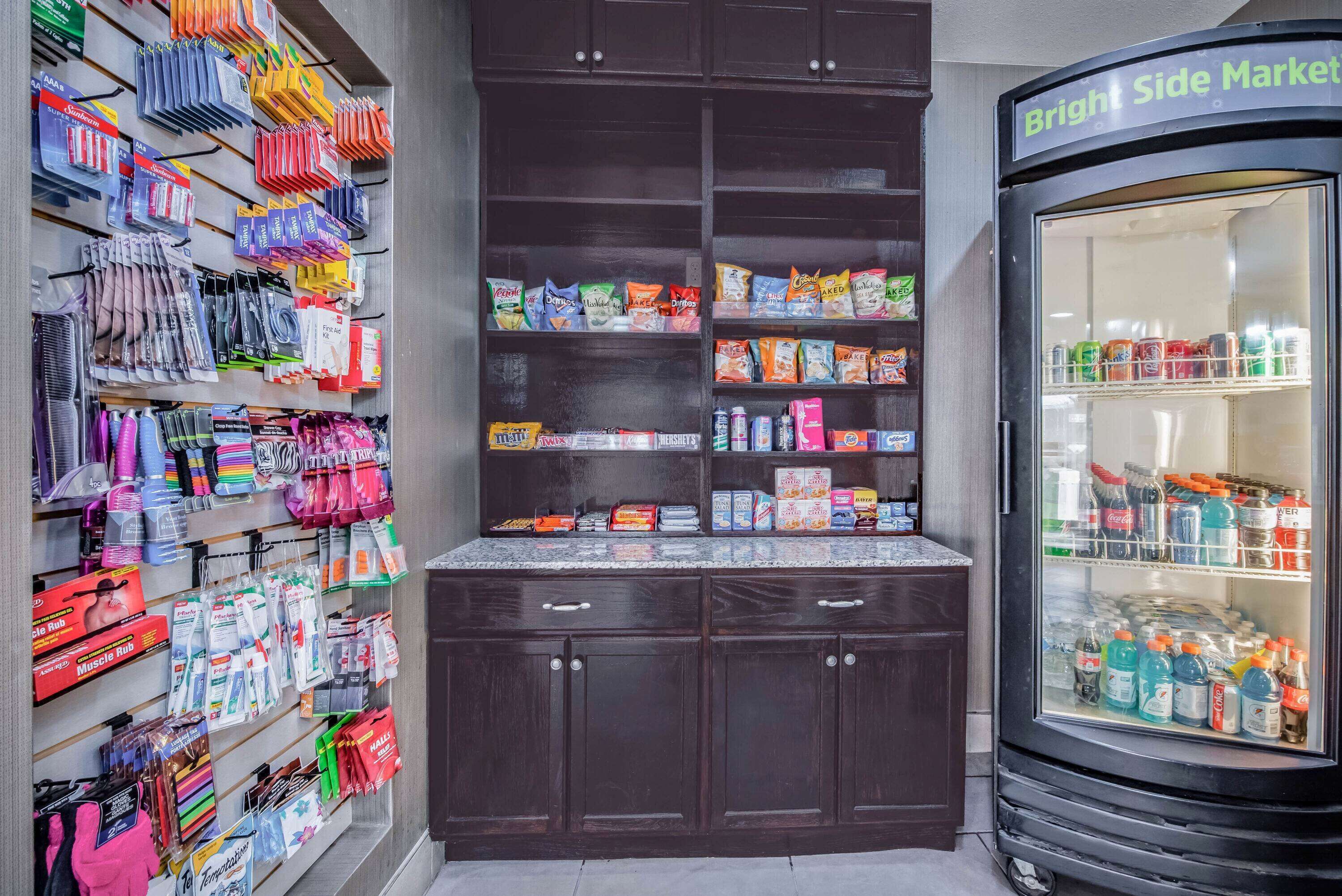 A section of a store with shelves stocked with various products, a display of colorful items on the left, and a refrigerated display case on the right.