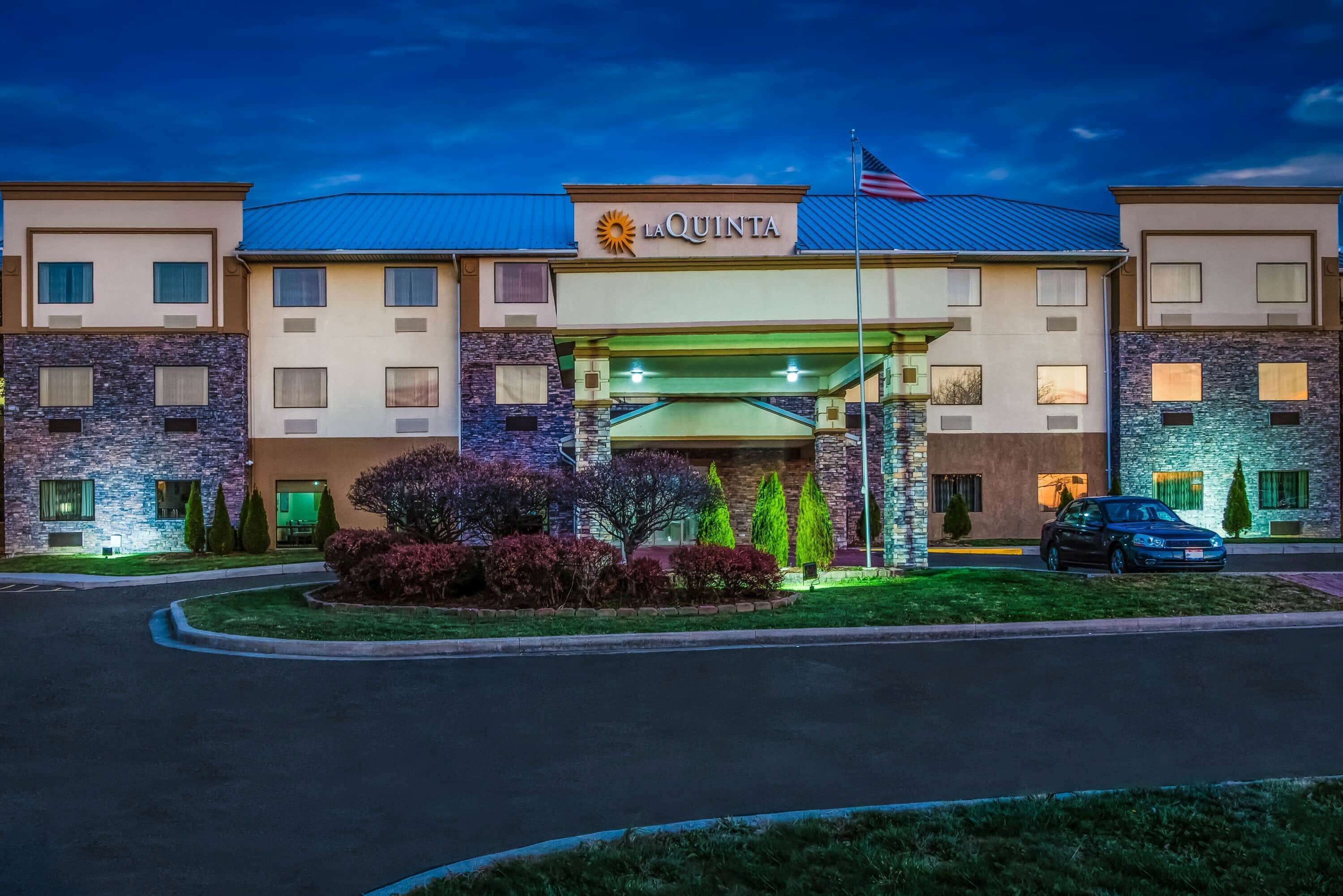 A hotel with a modern design, featuring a central entrance with a covered walkway, multiple floors, and a flag.
