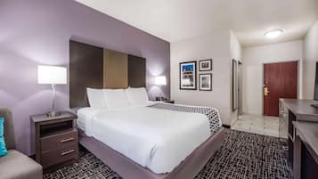 A hotel room with a large bed, a nightstand with a lamp, a desk with drawers, and a door.