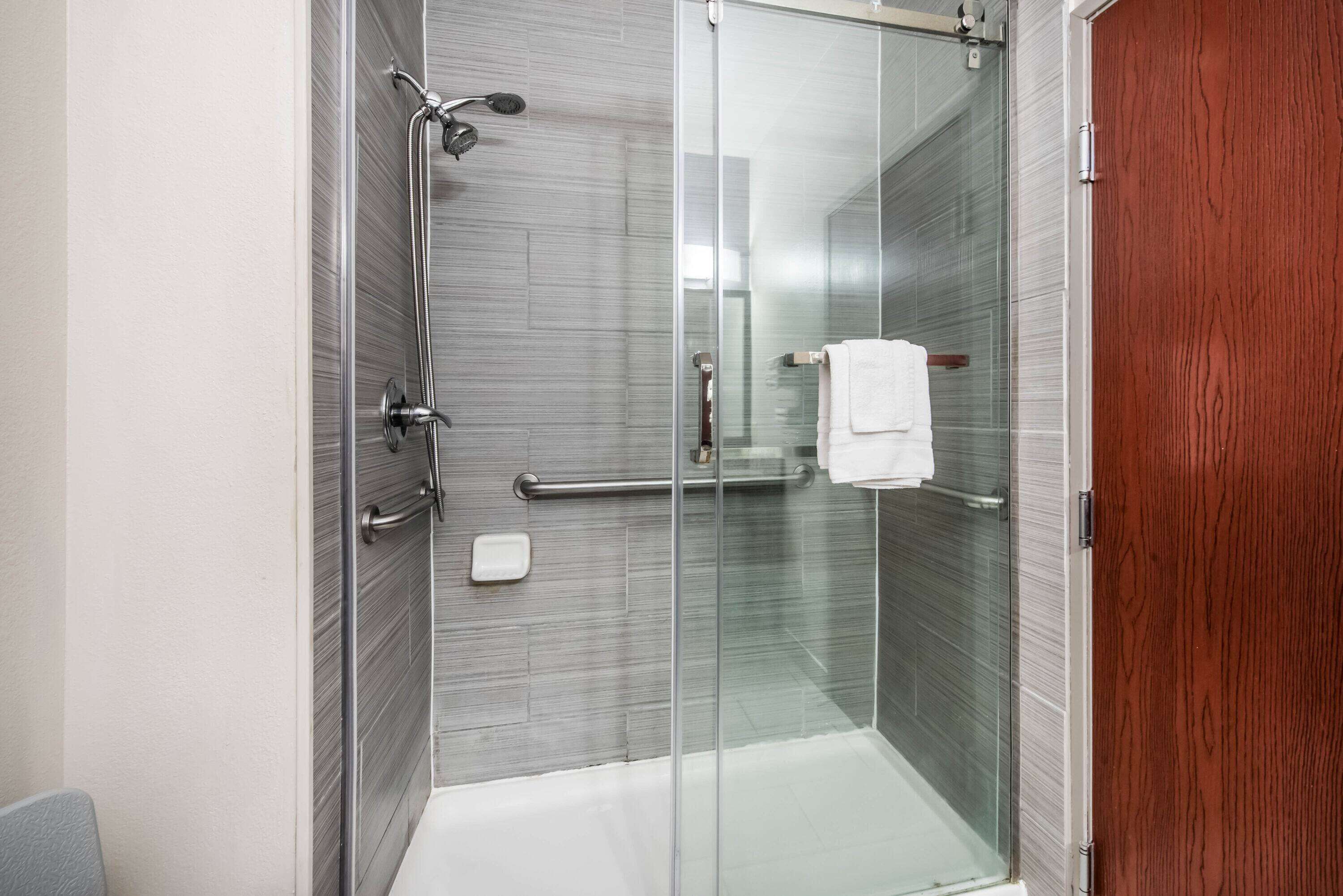 A modern shower with a glass door, a white towel hanging on the door handle, and a wooden door frame.