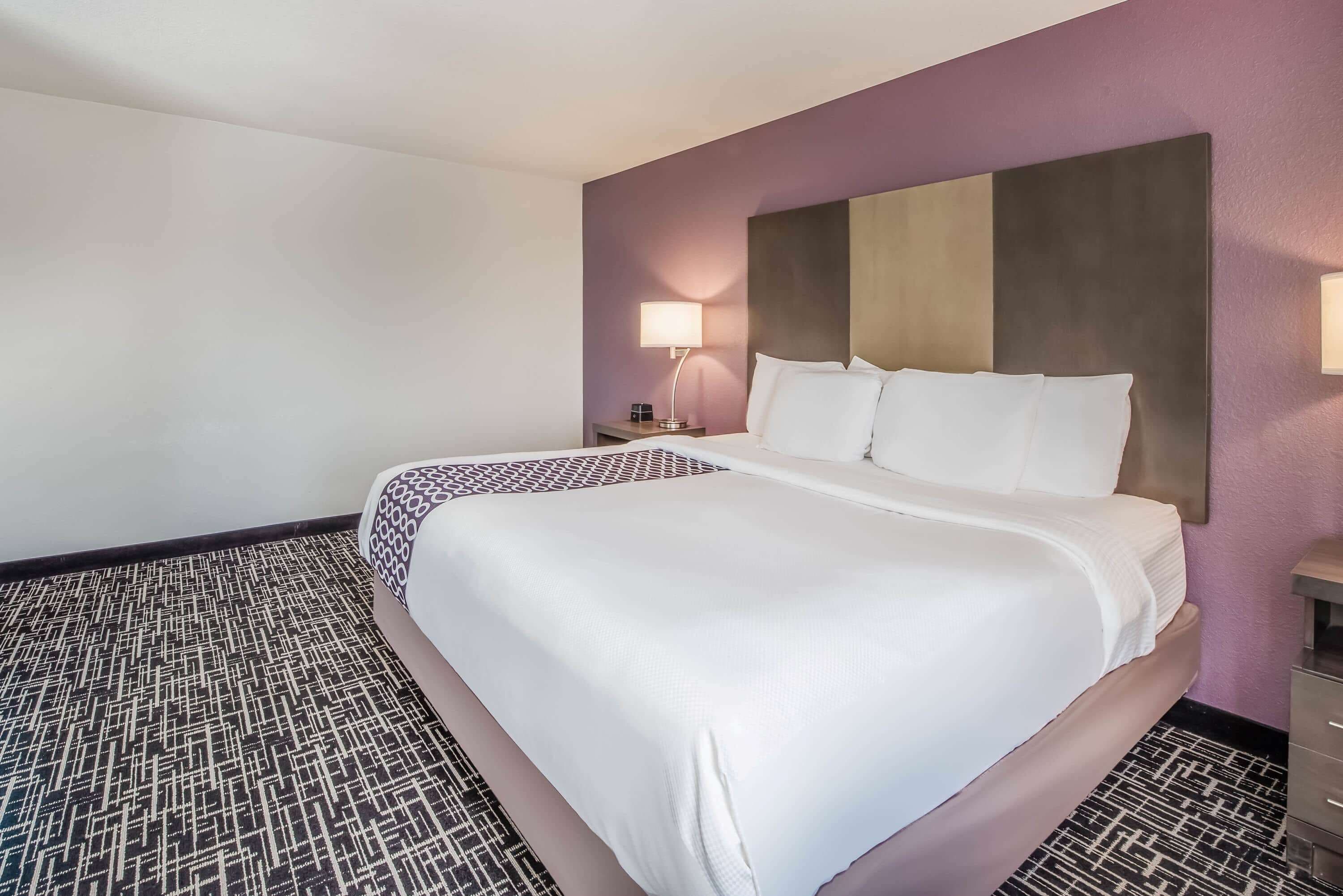 A hotel room with a large bed, a nightstand with a lamp, and a patterned carpet.