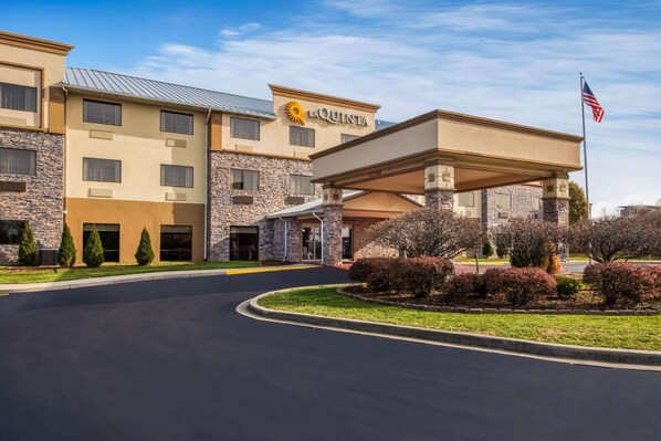 Un hotel La Quinta con fachada de piedra, un acceso cubierto y una bandera estadounidense.