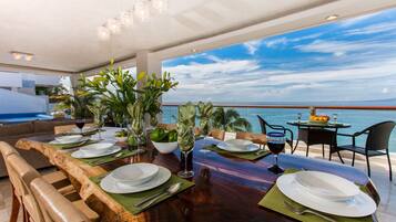 A dining area with a view of the ocean, featuring a wooden table set for a meal, chairs, and a view of the sea.