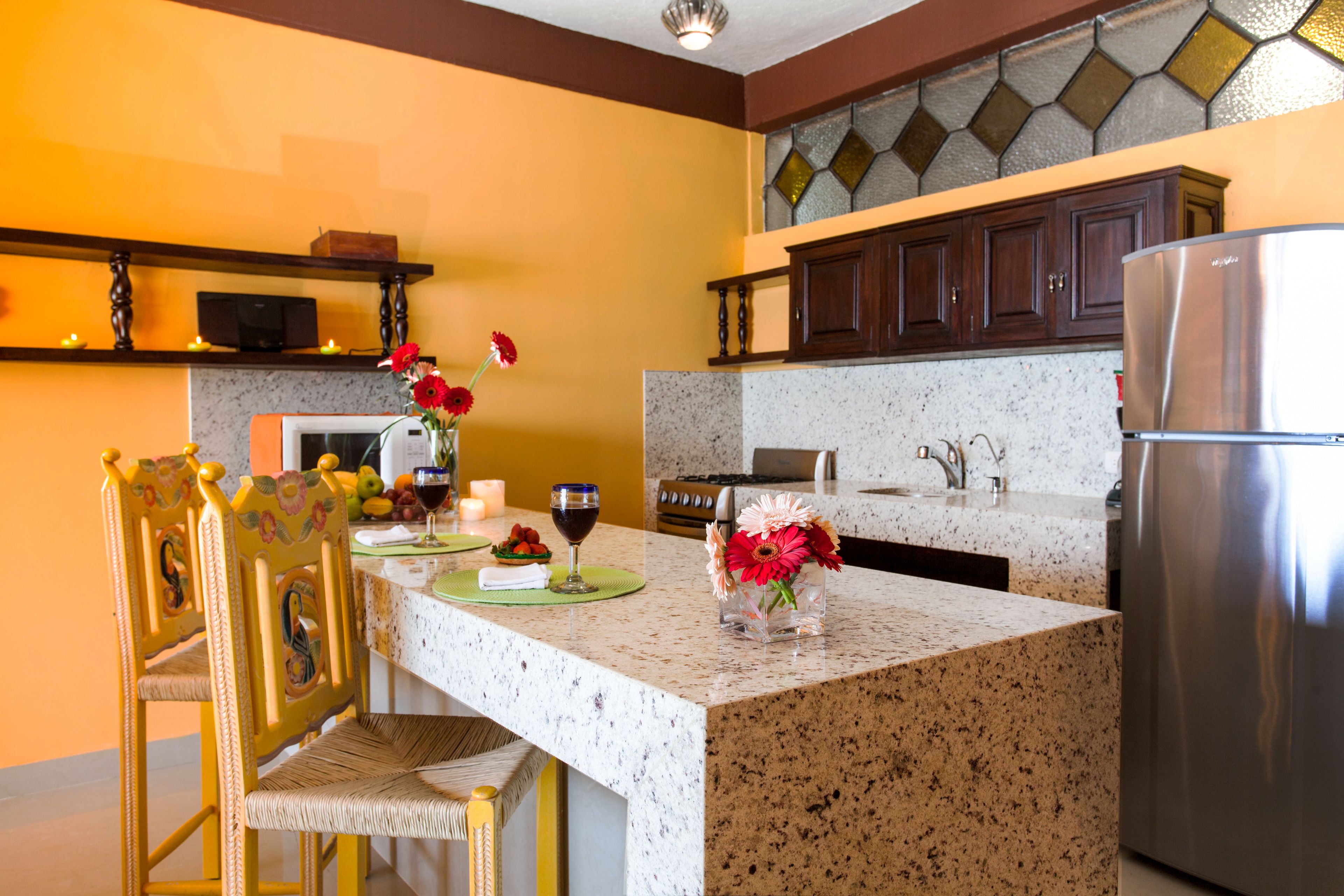 A kitchen with granite countertops, wooden cabinets, a stainless steel refrigerator, and a dining area with a chair and table.