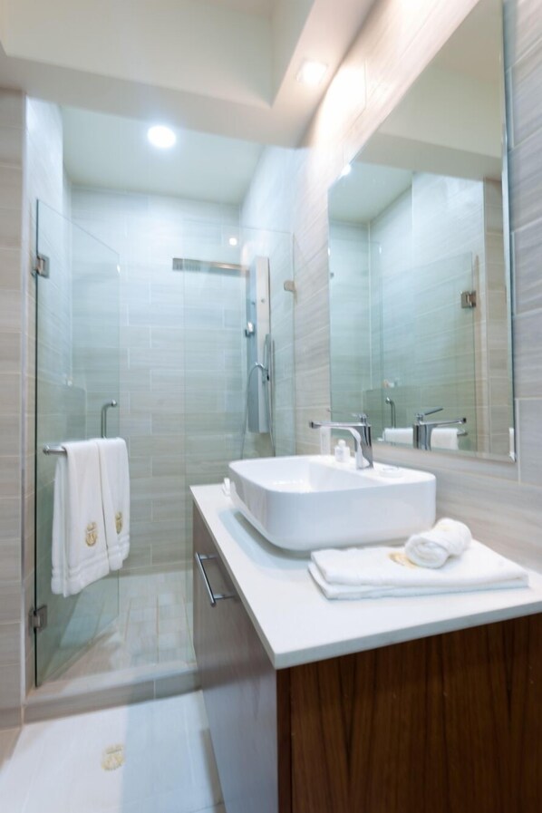 Un baño moderno con ducha envuelta en vidrio, un lavabo blanco y un espejo grande.