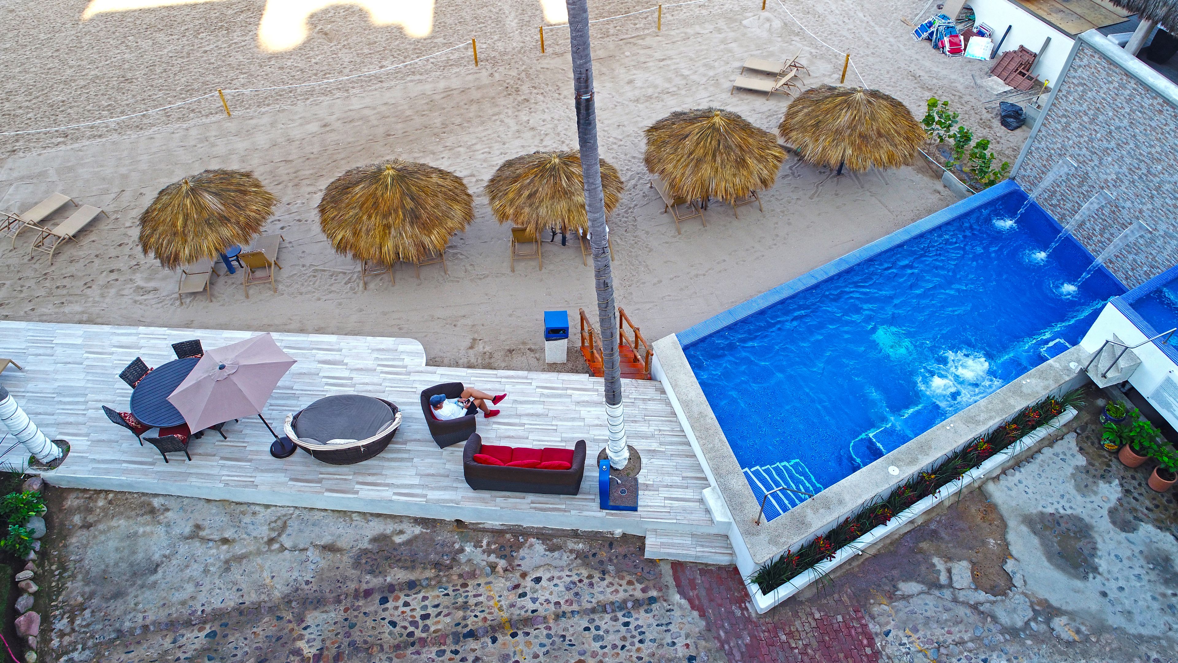 Un área de piscina en la azotea con sillones de descanso, sombrillas y una piscina.