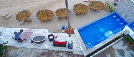 Un área de piscina en la azotea con sillones de descanso, sombrillas y una piscina.