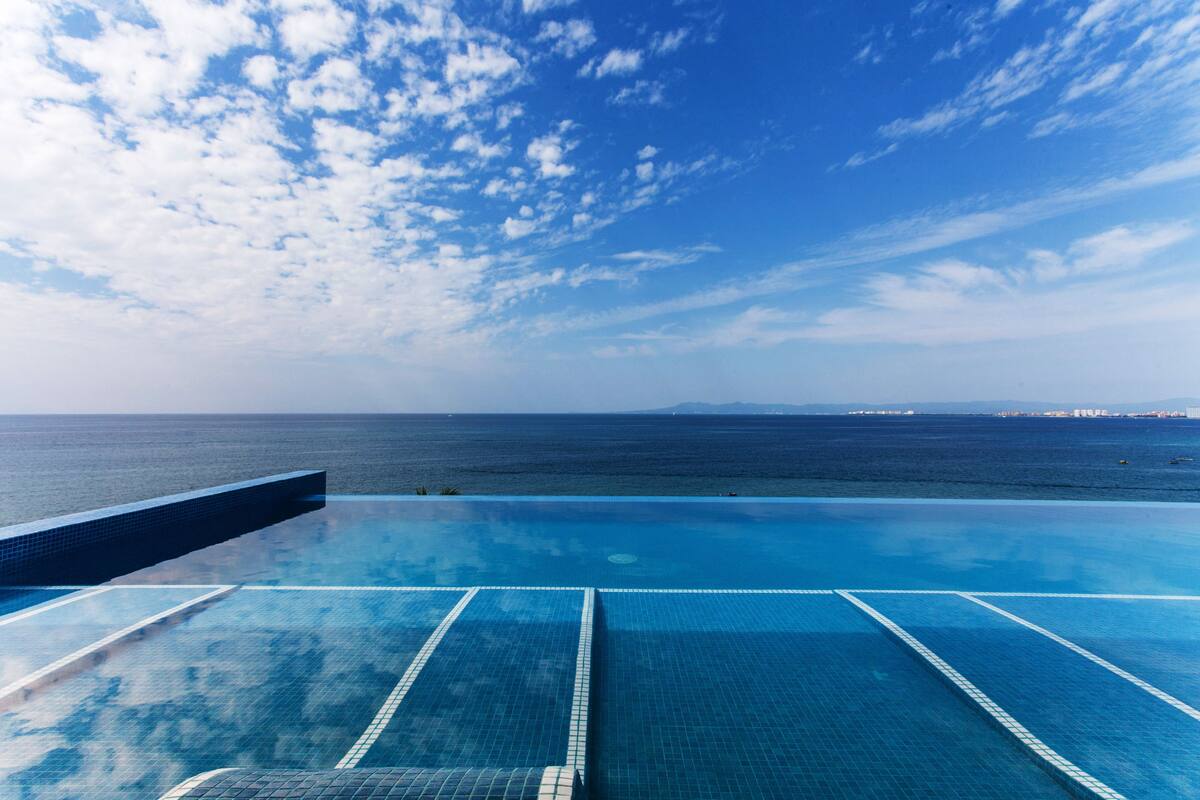 An infinity pool with clear blue water and a view of the ocean and distant horizon.