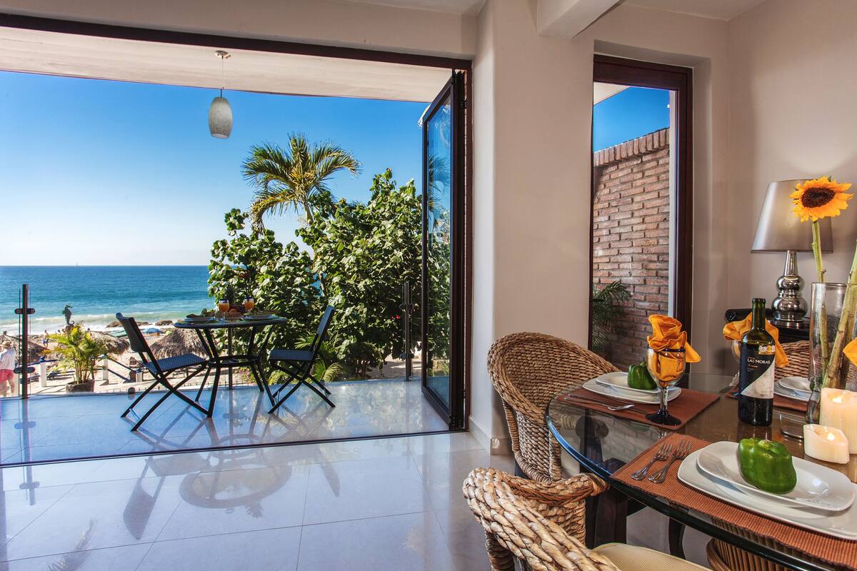 A dining area with a glass table, wicker chairs, and a view of the ocean.