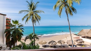 A beach view with palm trees, a sandy beach, and thatched umbrellas. - Vallarta Shores Beach Hotel (Puerto Vallarta)