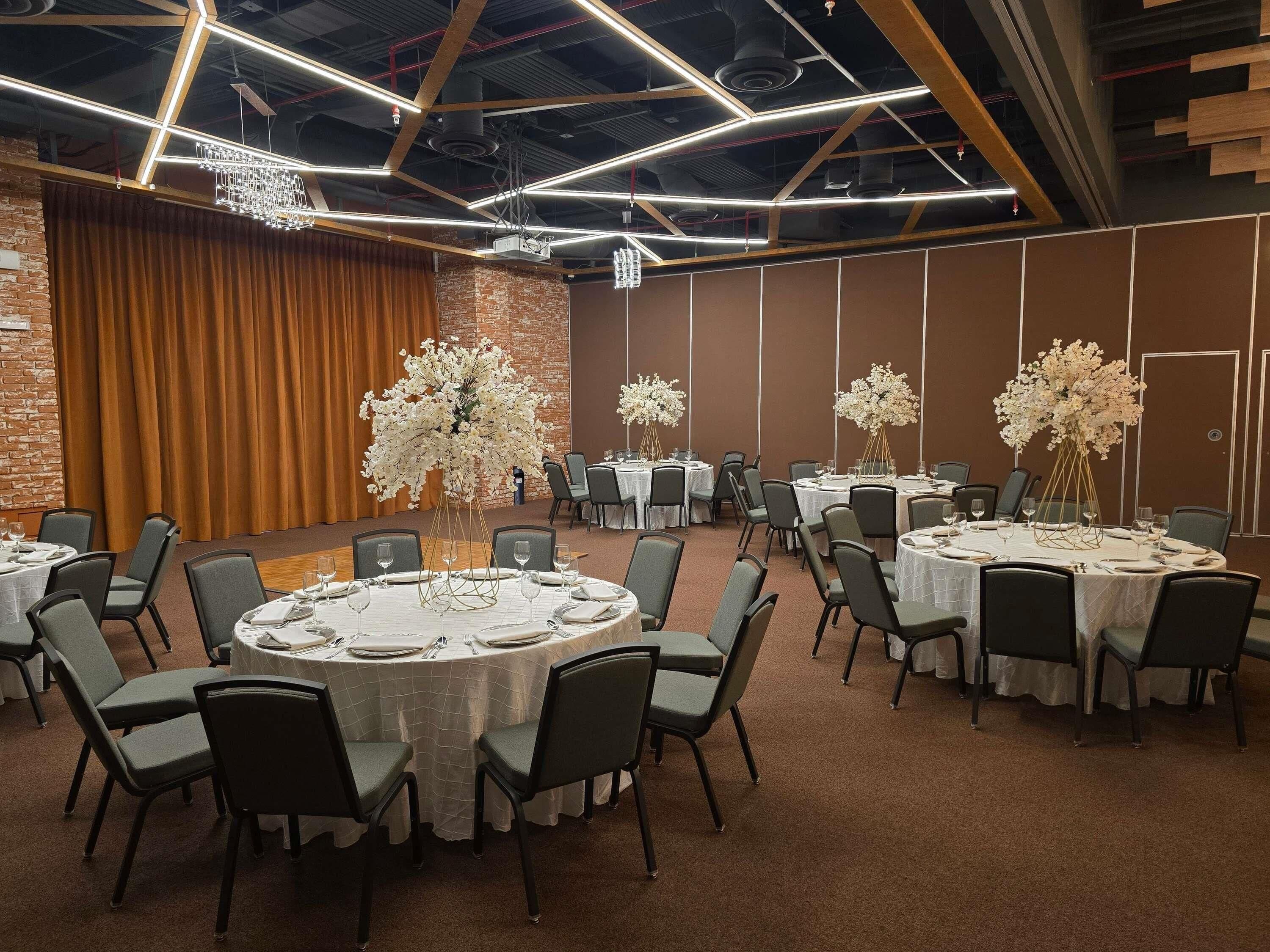 Uma sala de conferências com mesas redondas, cadeiras e centros de mesa florais.
