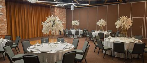 Uma sala de conferências com mesas redondas, cadeiras e centros de mesa florais.