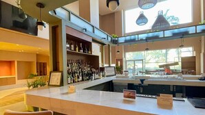 A modern bar area with a central island, bar stools, and hanging plants. - Novotel Monterrey Valle (San Pedro Garza García)