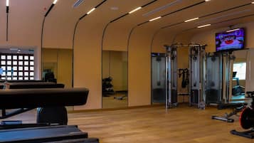 A gym with exercise equipment, a television screen, and a mirror.