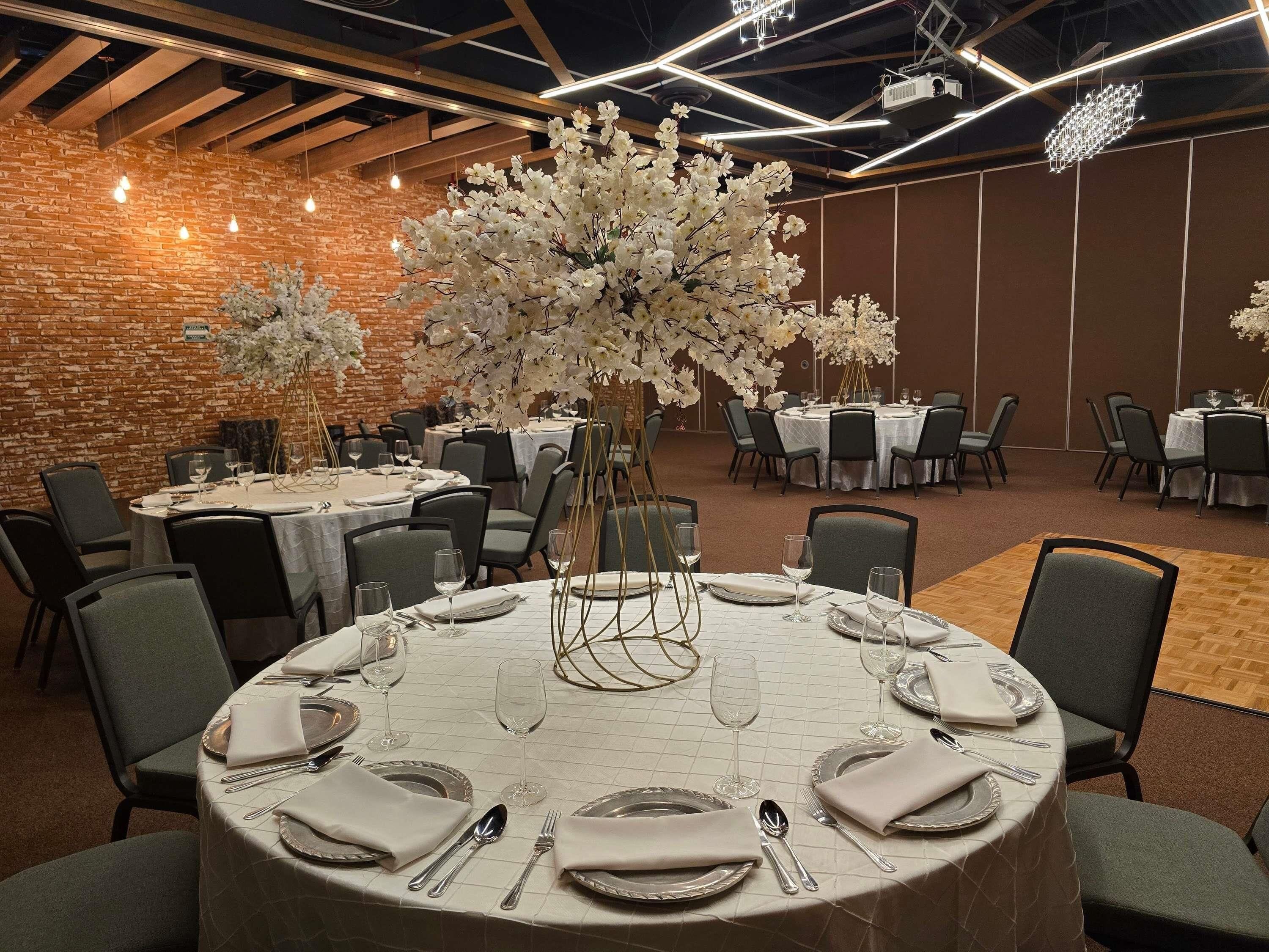 A banquet hall with round tables set for dining, featuring white tablecloths and silverware.