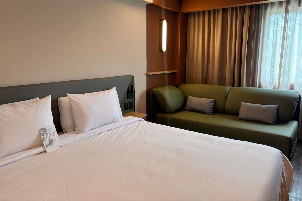 A hotel room with a large bed, a green sofa, and a window with curtains.
