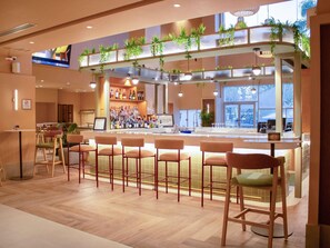 Uma área de bar com vários bancos, um balcão com garrafas e uma tela de televisão.