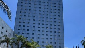 A hotel with a large pool, palm trees, and a tall building in the background. - Novotel Monterrey Valle (San Pedro Garza García)