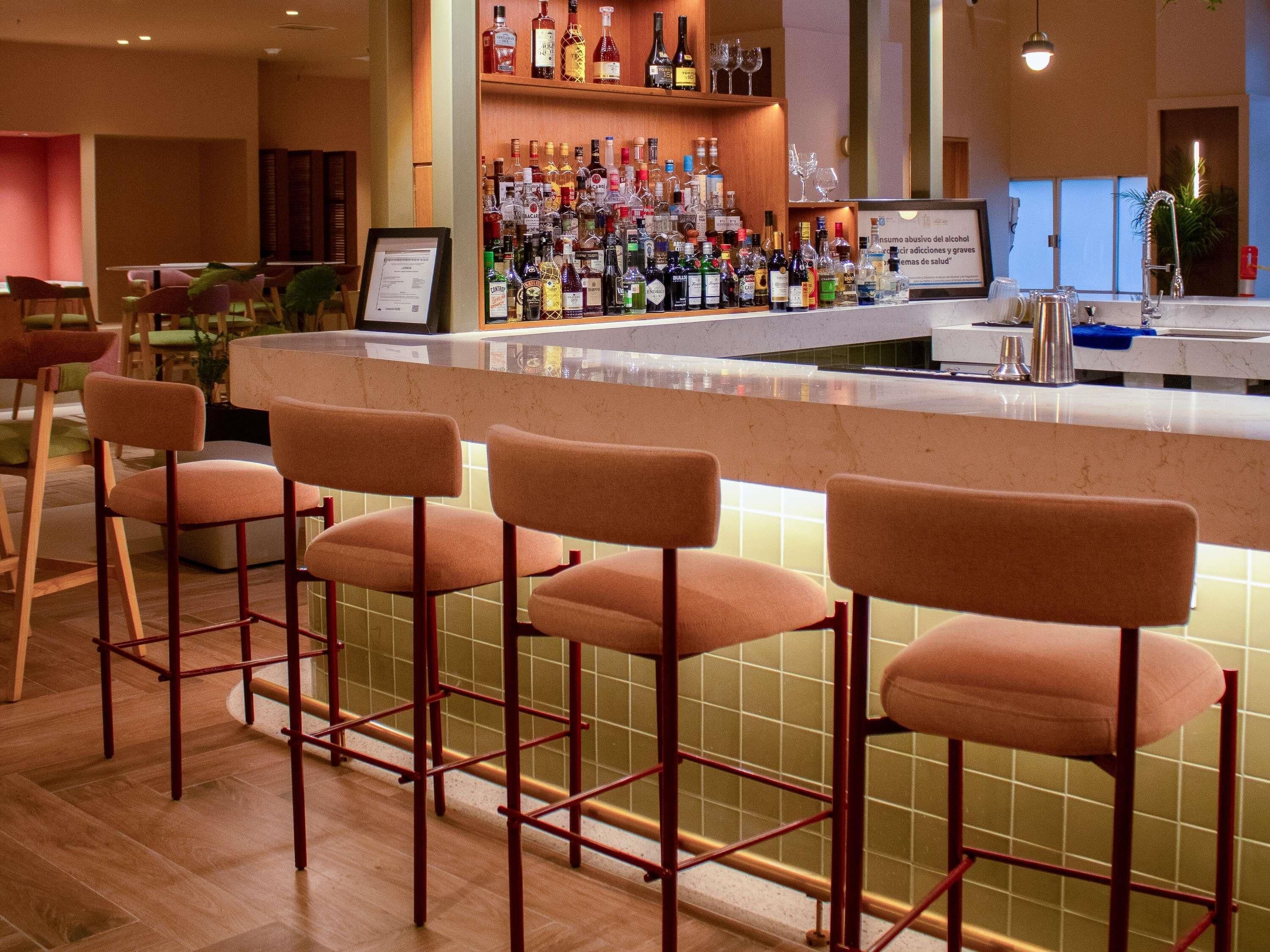 A bar area with multiple stools, a variety of liquor bottles, and a menu sign.