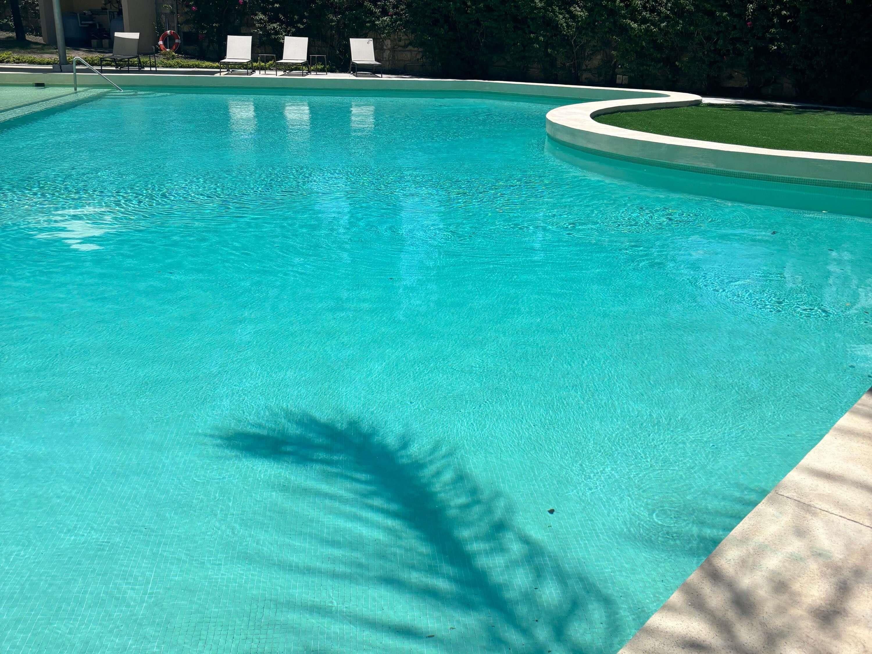 Una piscina cristalina con borde curvo, rodeada por un muro bajo y algunas sillas de descanso.
