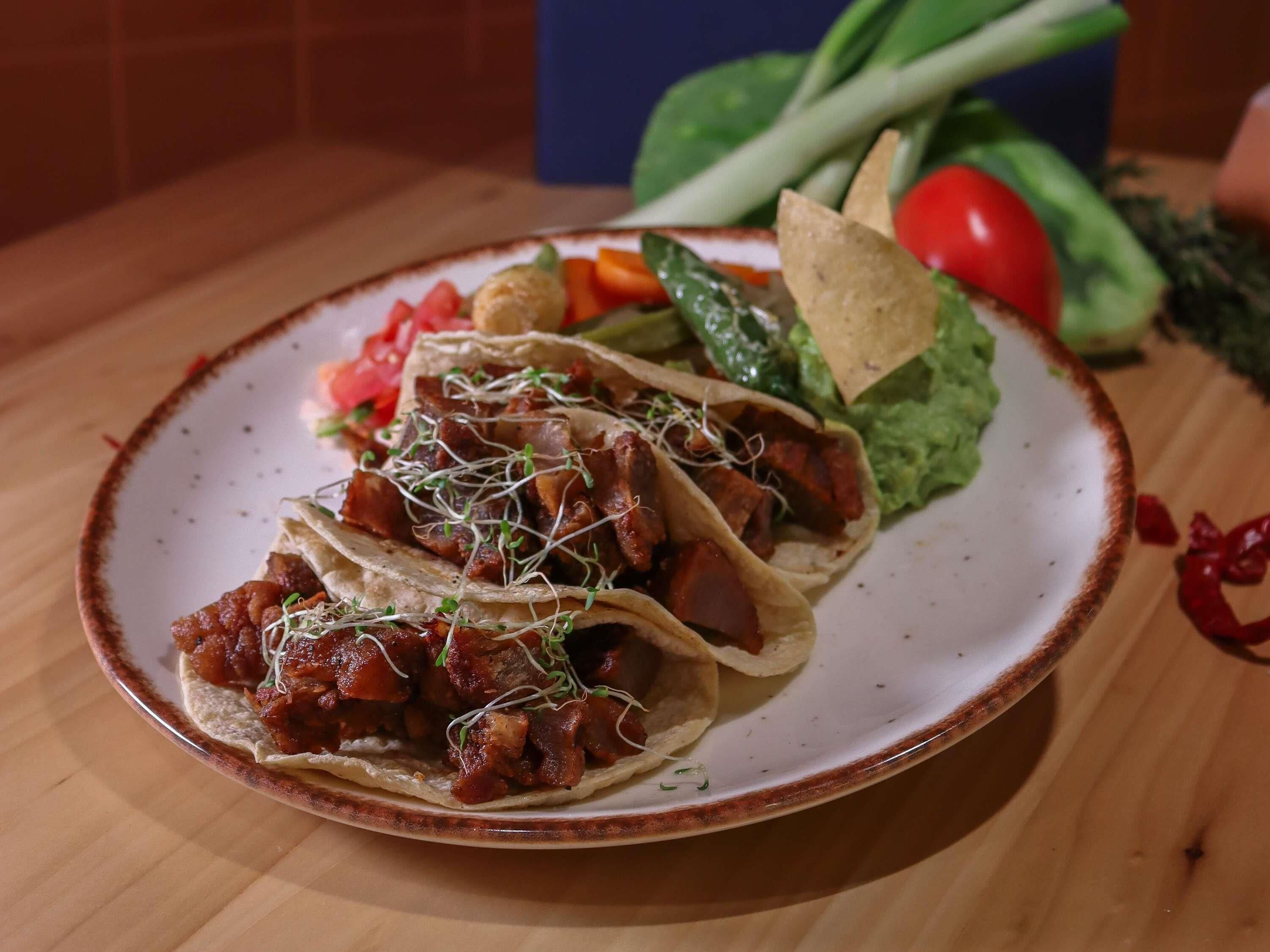 A plate with three tacos, a side of lettuce, and a small bowl of salsa.