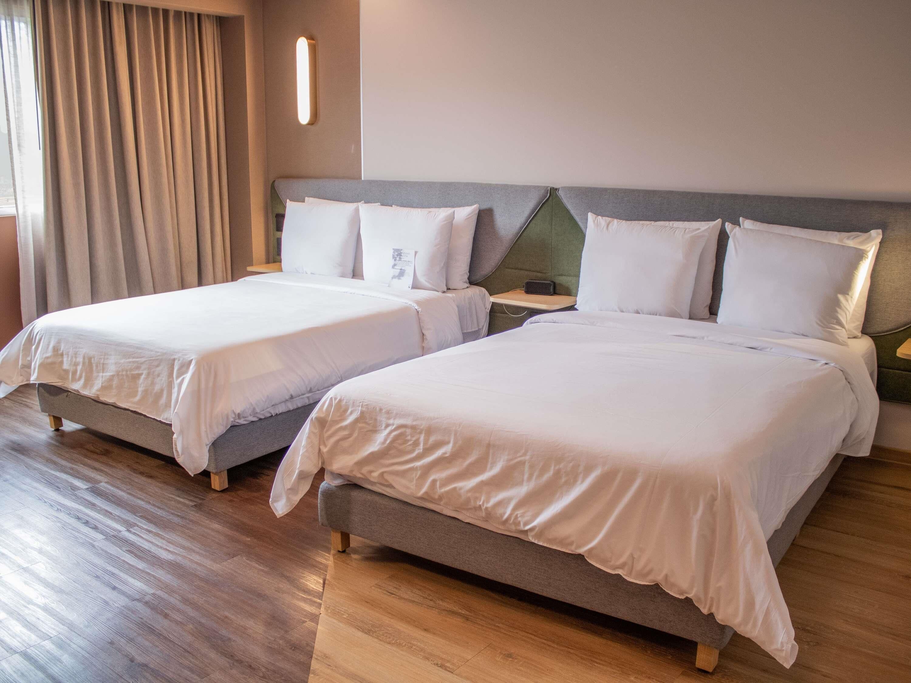 Two double beds with white linens, wooden flooring, a neutral color scheme, and a modern design.