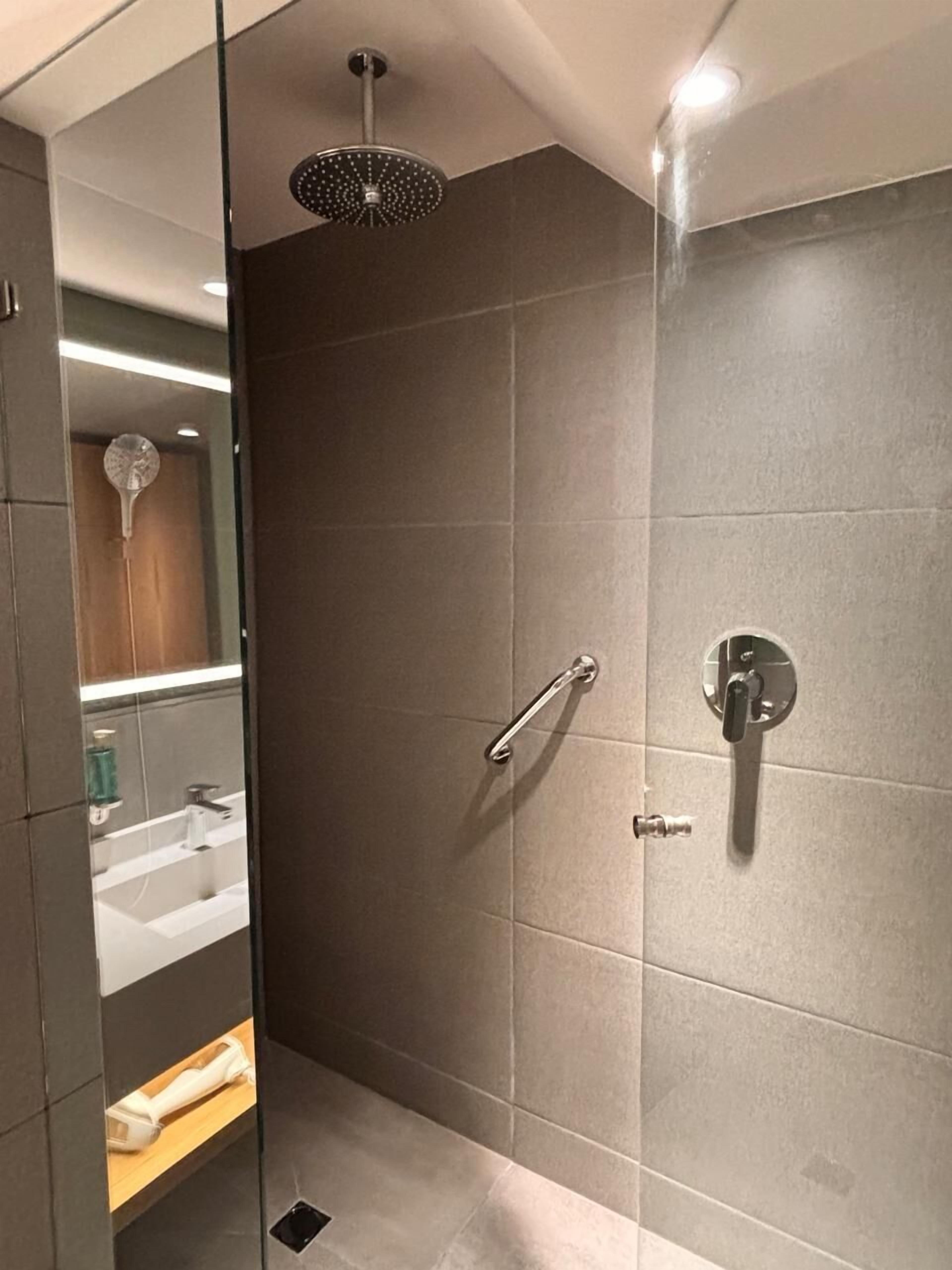 Um banheiro moderno com box de vidro, chuveiro manual, toucador com espelho e vaso sanitário.