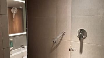 Um banheiro moderno com box de vidro, chuveiro manual, toucador com espelho e vaso sanitário.