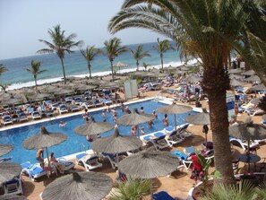 A pool area with lounge chairs and umbrellas, surrounded by palm trees and a view of the ocean.