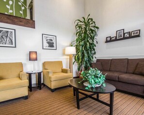 A hotel lobby with a brown sofa, a yellow armchair, a small round table, a floor lamp, and a large green plant. - Sleep Inn & Suites Niantic North (Niantic)