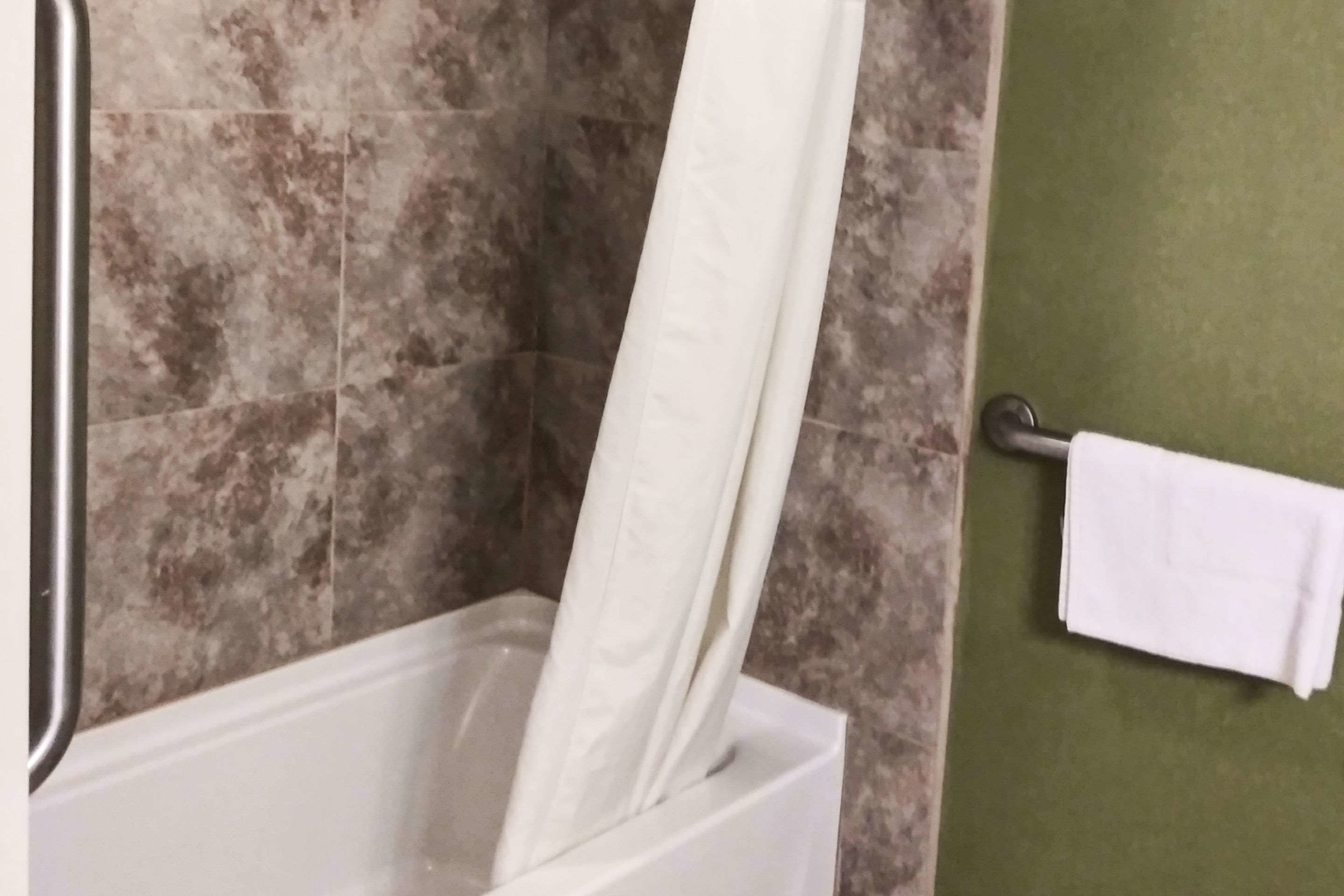 Un baño con cortina de ducha, toallero y pared de azulejos.