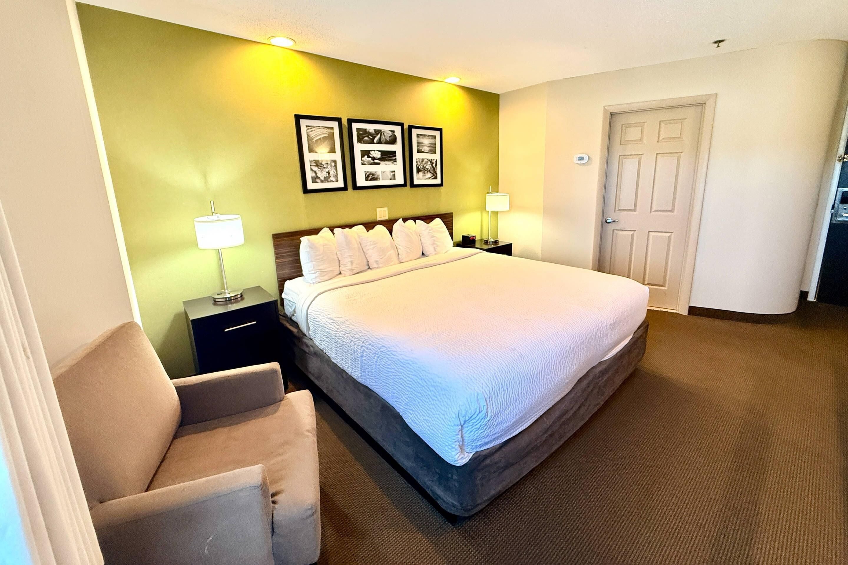 Una habitación de hotel con una cama, una silla, una mesita de noche, una lámpara y una puerta.