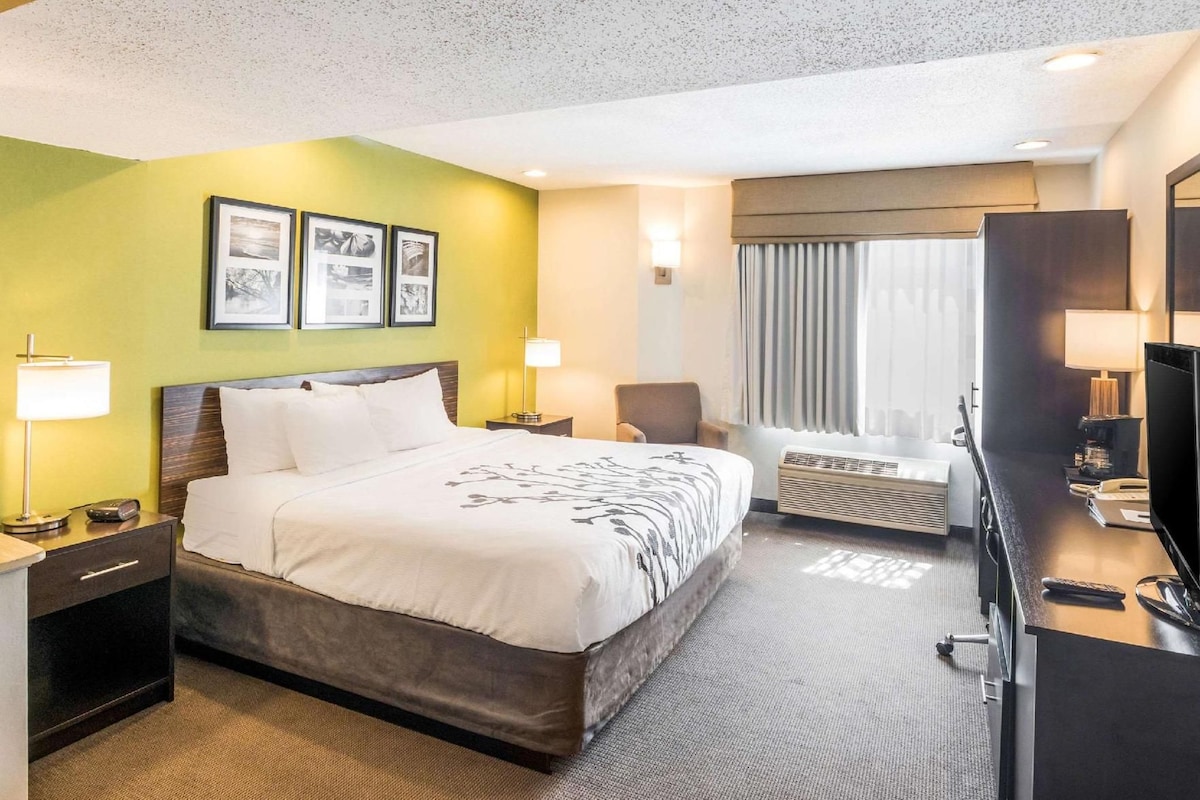 A hotel room with a bed, bedside tables, a desk with a TV, a chair, and a window with curtains.