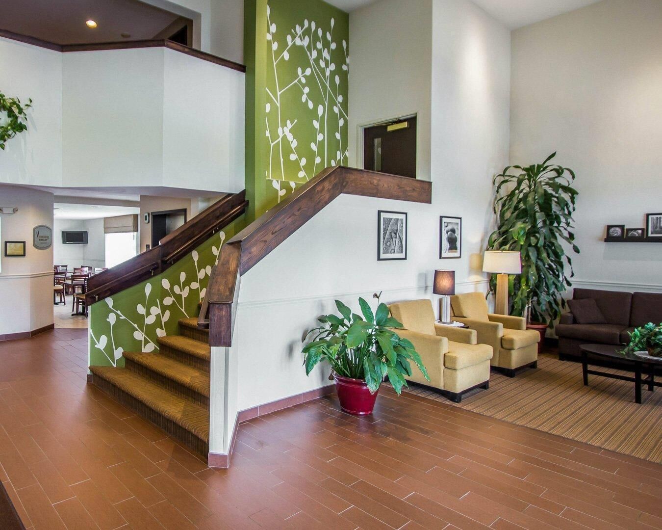 A spacious living area with a wooden staircase, comfortable seating, and a large potted plant.