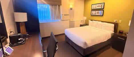 Quarto de hotel com cama, mesa de cabeceira, abajur e escrivaninha com cadeira.