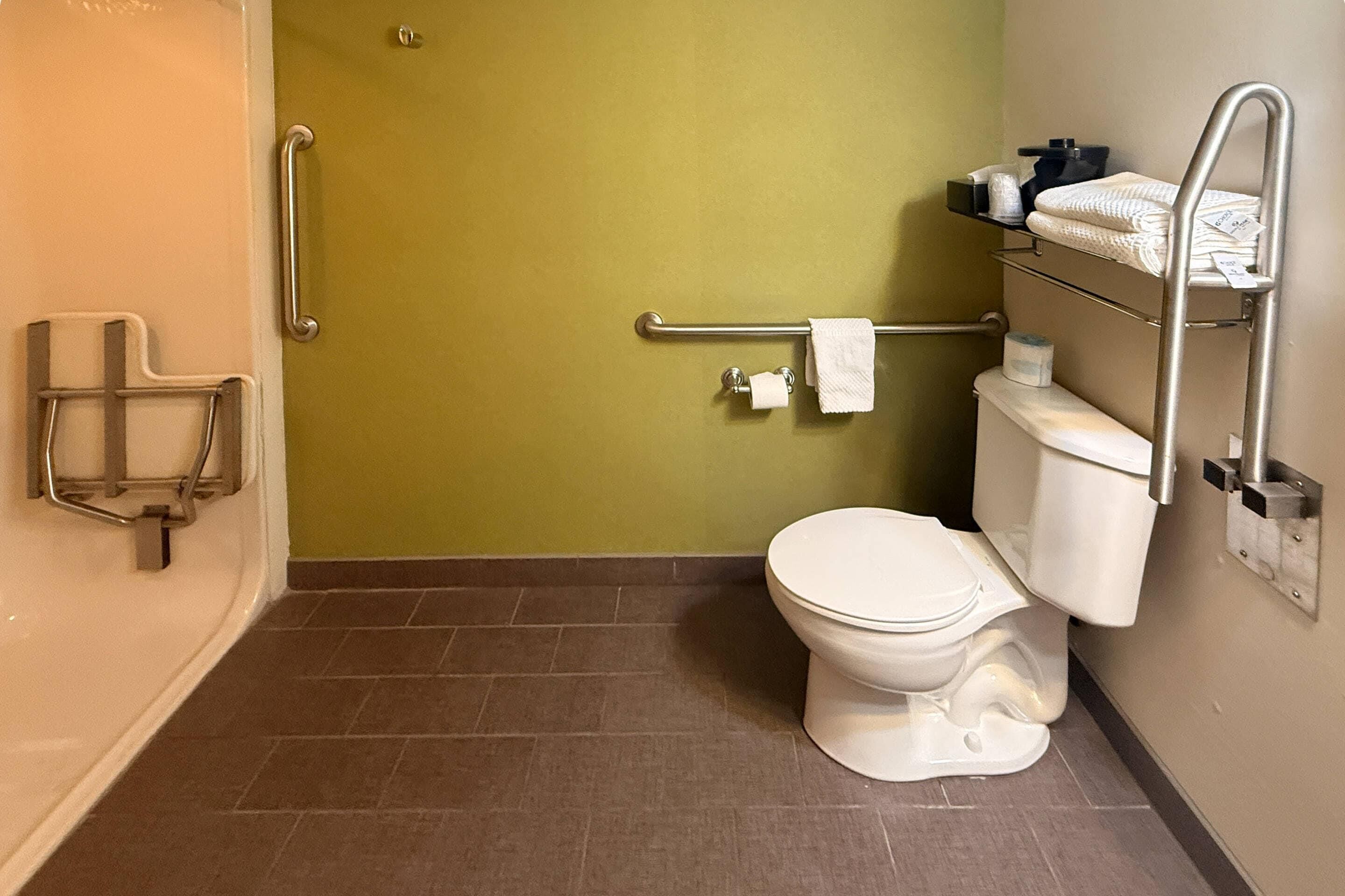 A bathroom with a white toilet, a grab bar, a towel rack, and a toilet paper holder.
