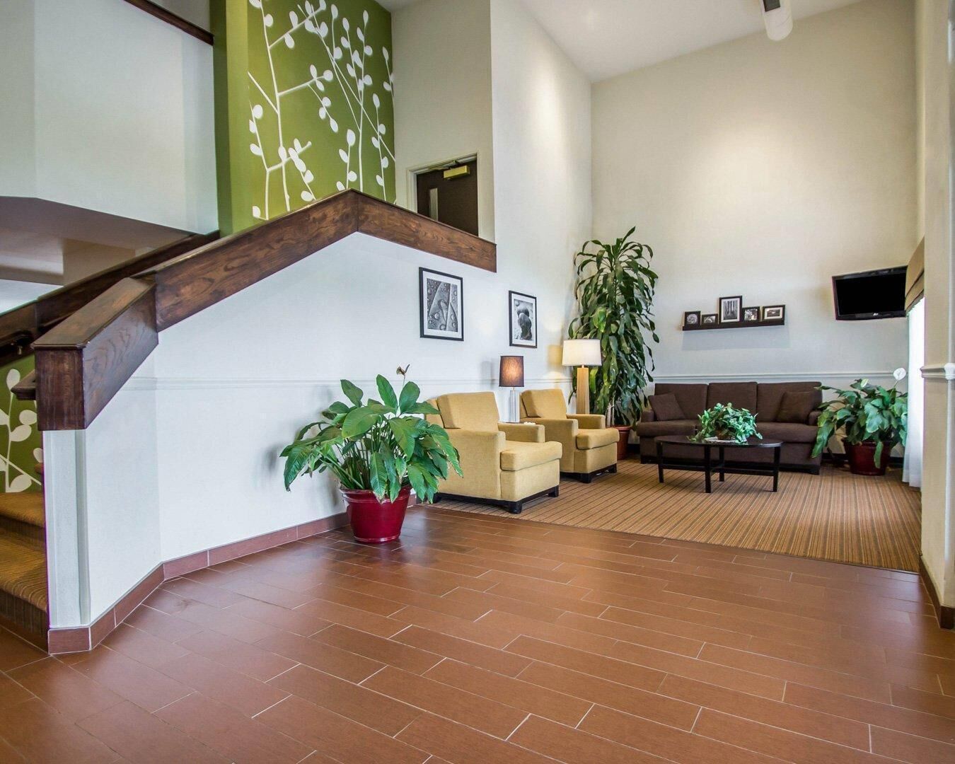 A spacious living area with a wooden staircase, comfortable seating, and a large potted plant.