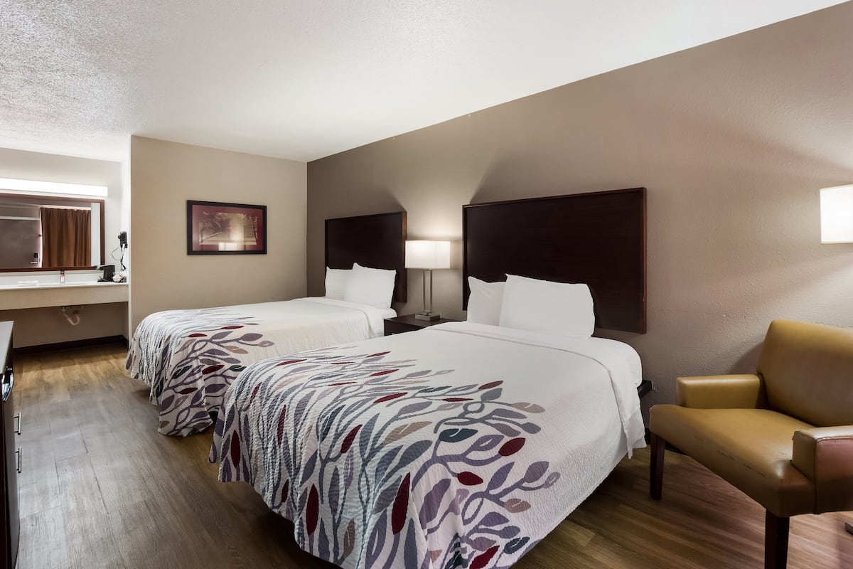 A hotel room with two beds, a desk, a chair, and a framed picture on the wall.