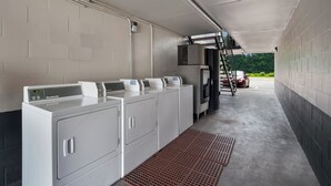 A laundry facility with industrial washing machines and dryers, a ventilation system, and a concrete floor. - Red Roof Inn Columbia, SC Airport (West Columbia)