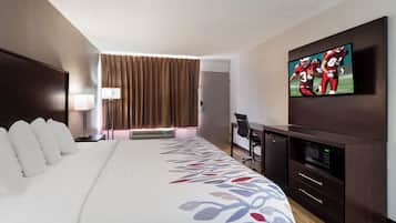 A hotel room with a large bed, a desk with a chair, a television, and an air conditioning unit.