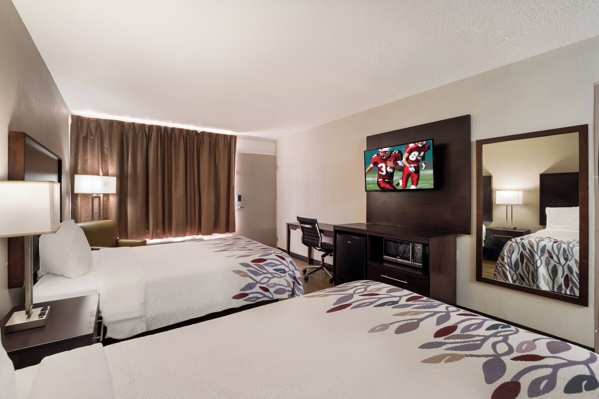 A hotel room with two beds, a desk, a TV, and a mirror.