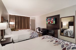 Una habitación de hotel con dos camas, un escritorio, un televisor y un espejo.
