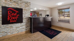 A Red Roof Inn reception desk with a stone wall backdrop, a wooden floor, and a window with blinds. - Red Roof Inn Columbia, SC Airport (West Columbia)