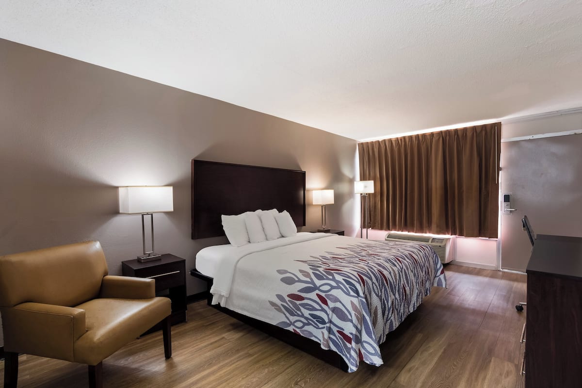 A hotel room with a bed, a chair, a nightstand, and a lamp.