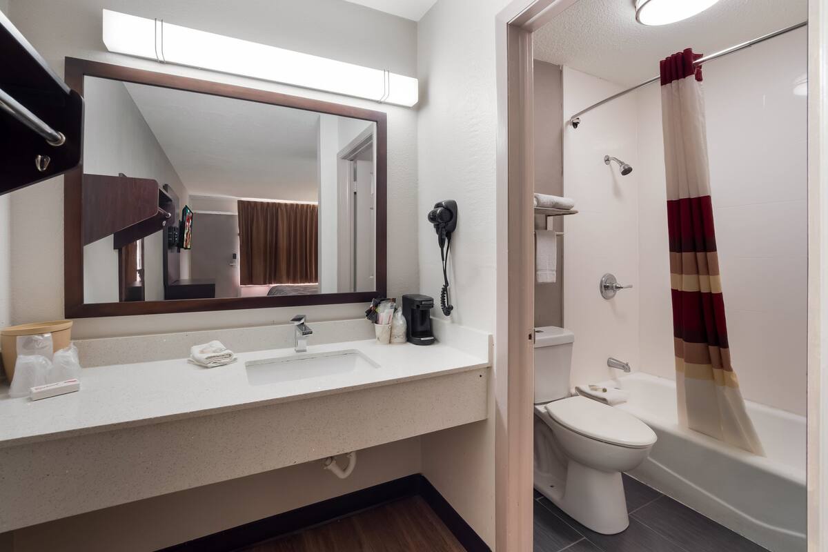 A modern bathroom with a white sink, a large mirror, a hairdryer, and a shower with a red curtain.