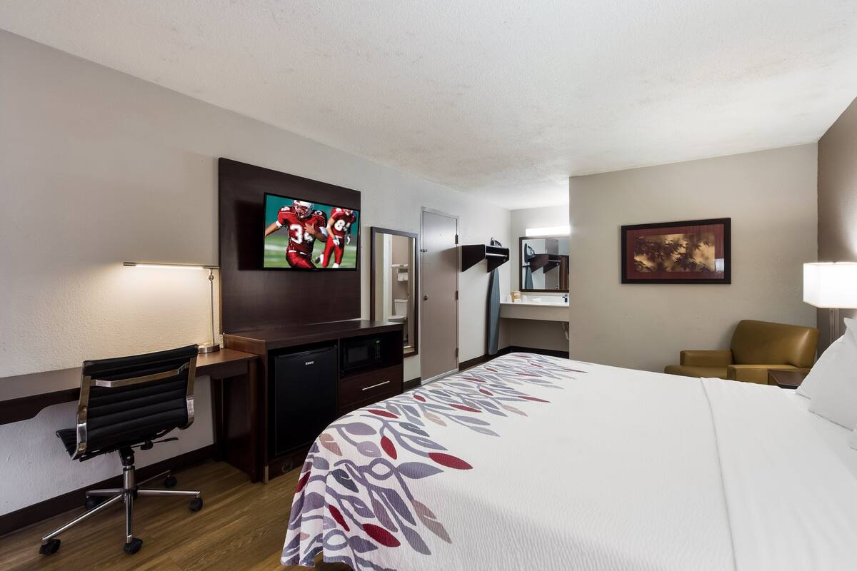 A hotel room with a bed, desk, chair, TV, and a bathroom.