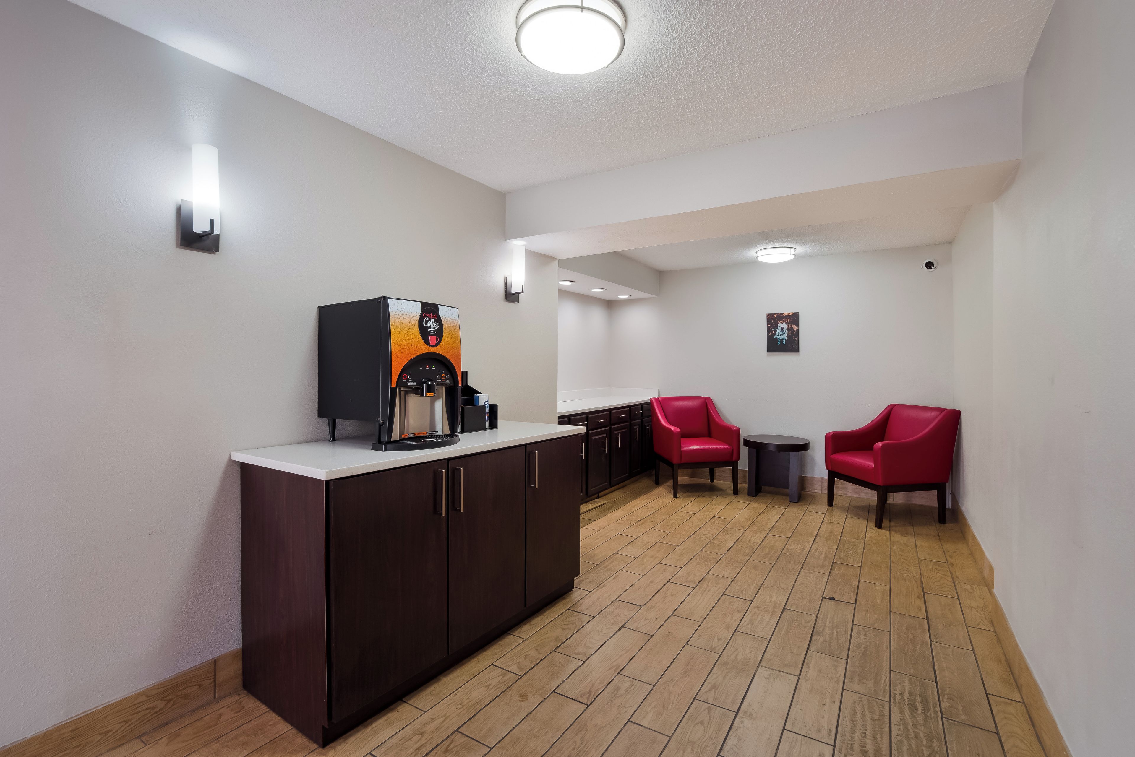 A modern kitchen with a coffee machine, two red chairs, and a small table.