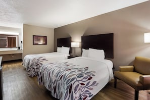 A hotel room with two beds, a desk, a chair, and a framed picture on the wall. - Red Roof Inn Columbia, SC Airport (West Columbia)