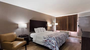 Een hotelkamer met een bed, een stoel, een nachtkastje en een lamp.